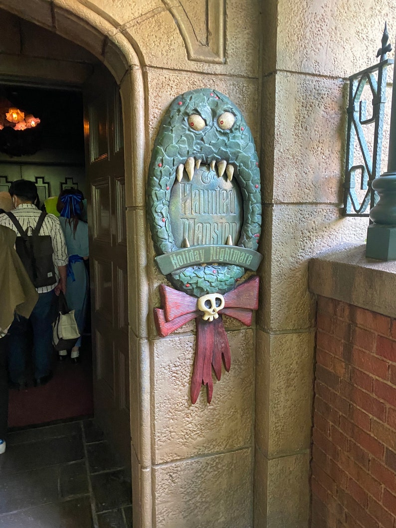 Może przedstawiać: Zielone, potworne usta z tabliczką z napisem "The Haunted Mansion Holiday Nightmare".