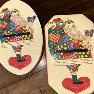 May include: Two oval-shaped Christmas ornaments featuring a patchwork Santa Claus holding a bird. The ornaments are white with red trim and a glittery finish.