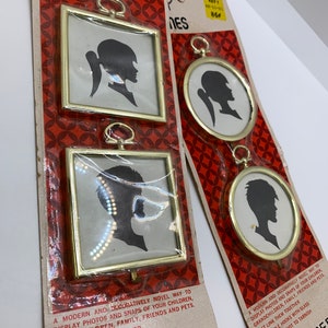May include: Three gold-toned picture frames with silhouette images of people. The frames have a hook on the top and are designed to be linked together. The packaging includes the text "DILLAC FRAMES" and "NO. 200-2".
