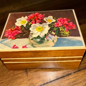 May include: A wooden music box with a floral design on the lid. The flowers are white and pink and are in a clear vase. The music box is closed.