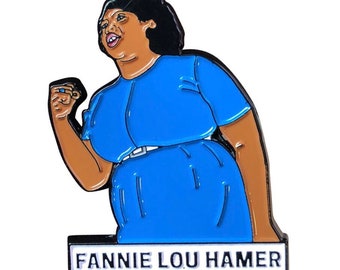 May include: Enamel pin featuring a stylized illustration of Fannie Lou Hamer in a blue dress, with a raised fist. The pin has a white border with the name "FANNIE LOU HAMER" in black text.