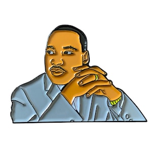 May include: Enamel pin featuring a portrait of a man with brown skin, a mustache, and a gray suit. The pin has gold accents and a green ring. The man's hands are clasped in front of him.