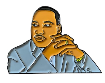 May include: Enamel pin featuring a portrait of a man with brown skin, a mustache, and a gray suit. The pin has gold accents and a green ring. The man's hands are clasped in front of him.