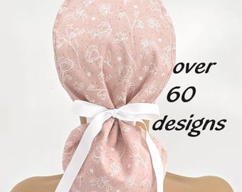 May include: A pink scrub cap with a white floral pattern and a white ribbon tie. The text "over 60 designs" is printed in black on the right side of the cap. The cap is designed to be worn on the head.