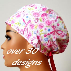May include: A white surgical scrub cap with a pink floral pattern, pink ribbons, and the words "Love", "Hope", and "Faith". The cap has a pink ribbon tie and the text "over 30 designs".