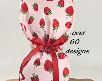 May include: A pink surgical scrub hat with a strawberry print and red ribbon ties. The hat has white polka dots and the text "over 60 designs" is visible.
