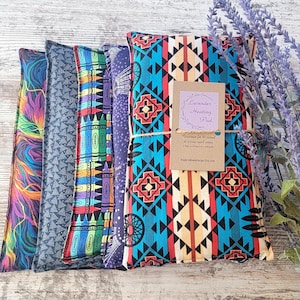 May include: A stack of colorful, patterned heating pads. The pads feature various designs, including a vibrant abstract pattern, geometric shapes, and a Southwestern-inspired print. A tag reads "Lavender Heating Pad."