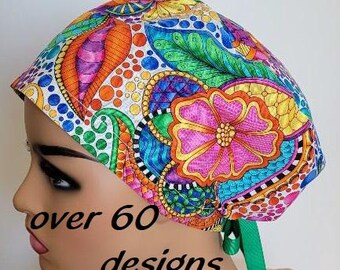 May include: A colorful patterned scrub cap featuring a vibrant floral design in shades of pink, orange, yellow, and blue. The cap has a green tie and the text "over 60 designs" is visible.