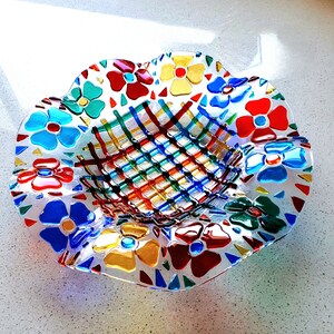 以下が含まれることがあります： 花柄のデザインが施された装飾ガラスボウル。ボウルは、縁に赤、青、黄、緑のカラフルな花が咲く透明なベースが特徴です。中央にはさまざまな色の織り模様があります。ボウルはユニークな芸術作品です。