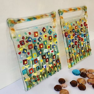 Op de afbeelding: Twee snijplanken van glas met een bloemenontwerp. De planken zijn gemaakt van helder glas met kleurrijke moza&iuml;ektegels in tinten rood, geel, blauw en groen. De tegels zijn gerangschikt in een patroon van bloemen en stengels.
