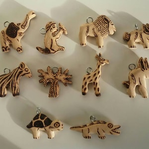 May include: A set of ten wooden animal charms, each with a different animal design, including a giraffe, zebra, elephant, monkey, turtle, crocodile, donkey, lion, rabbit, and a palm tree. The charms are all hand-painted and have a rustic, natural look.