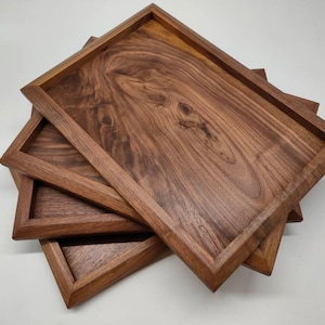 Puede incluir: Tres bandejas de madera apiladas una encima de la otra. Las bandejas están hechas de madera de nogal y tienen un acabado natural. Las bandejas son de forma rectangular y tienen un borde ligeramente elevado.