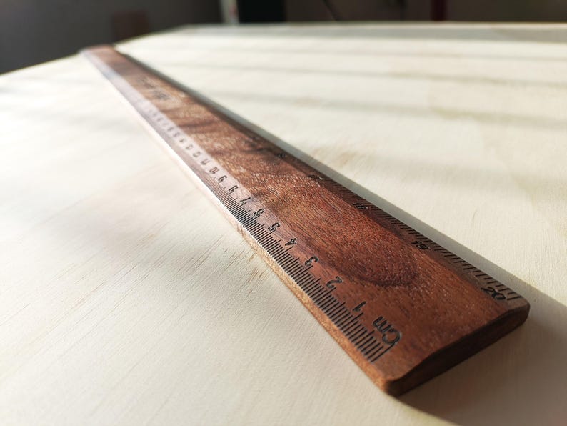 May include: A straight wooden ruler with a dark brown wood grain finish. The ruler features clearly marked black measurement increments along the edge, with the text 'cm' visible near the 1-centimeter mark and numbers extending up to 20 cm.