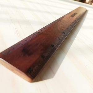 May include: A dark brown wooden ruler featuring clearly marked black metric measurements along its edge. The ruler displays a smooth, polished finish with visible wood grain patterns and the text "SPRING WOOD" printed near the top end.
