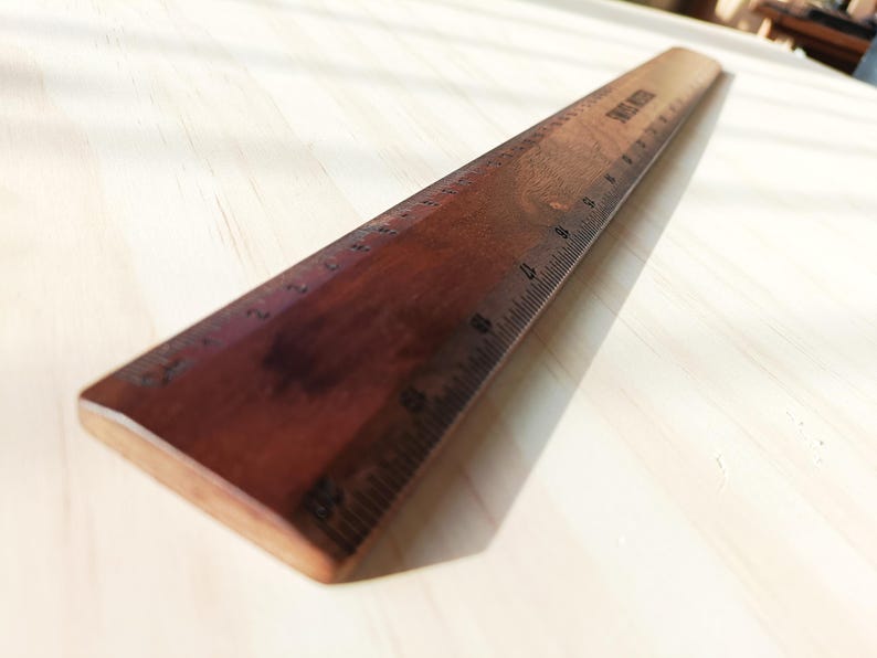 May include: A dark brown wooden ruler featuring clearly marked black metric measurements along its edge. The ruler displays a smooth, polished finish with visible wood grain patterns and the text "SPRING WOOD" printed near the top end.