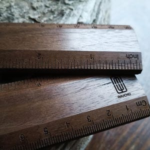 May include: Two dark brown wooden rulers with visible wood grain. The top ruler features imperial markings in inches, while the bottom ruler displays metric markings in centimeters. A black logo with the text IMUCHU is printed on the bottom ruler.