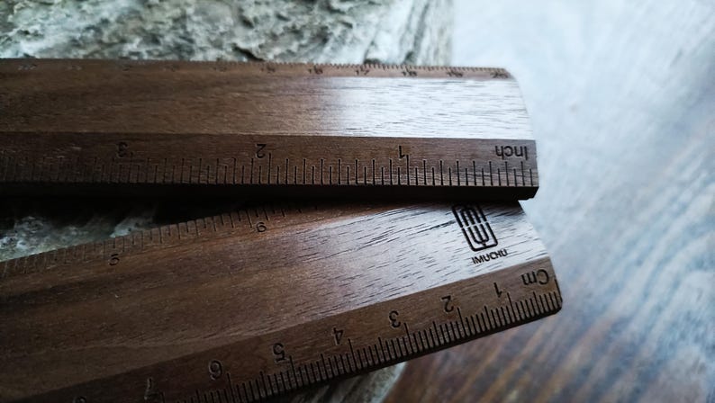 May include: Two dark brown wooden rulers with visible wood grain. The top ruler features imperial markings in inches, while the bottom ruler displays metric markings in centimeters. A black logo with the text IMUCHU is printed on the bottom ruler.