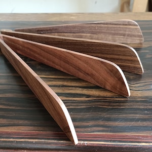 Può includere: Un set di quattro pinze da cucina in legno marrone scuro con finitura liscia. Le pinze sono collegate a un'estremità da una piccola cerniera metallica, che permette alle quattro lame in legno piatte e allungate di aprirsi a ventaglio.
