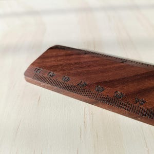 May include: A dark brown wooden ruler featuring clearly etched black measurement markings. The ruler displays numerical increments starting from 43 and continuing upward, with a visible grain pattern throughout the wood surface.