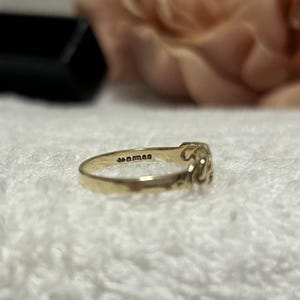 May include: A gold ring with an ornate design. The ring is set against a soft, white background. The ring has the text "44man" engraved on the inside.