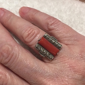 Könnte beinhalten: Ein silberner Ring mit einem rechteckigen roten Korallen-Stein, der in einen Rahmen aus Markasit-Steinen gefasst ist.
