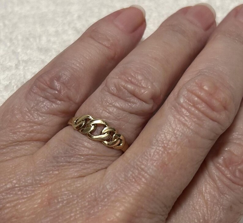 May include: A gold-colored ring with a chain link design. The ring is worn on a finger and has a polished finish. The ring is a piece of jewelry.