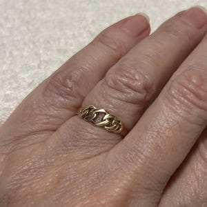 May include: A gold ring with a chain link design. The ring is made of yellow gold and features a series of interconnected links. The ring is worn on a finger.