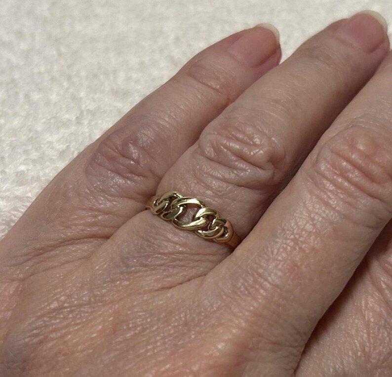May include: A gold ring with a chain link design. The ring is made of yellow gold and features a series of interconnected links. The ring is worn on a finger.