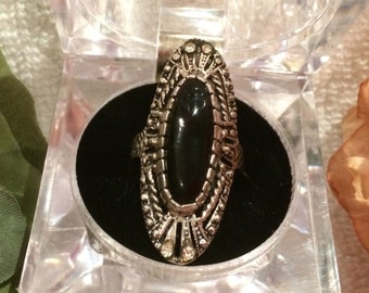 May include: A silver ring with a large black oval gemstone set in a filigree design. The ring is in a small black velvet box.