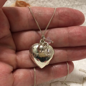 May include: A silver heart-shaped locket necklace with a silver bell charm and pink and clear crystal beads.
