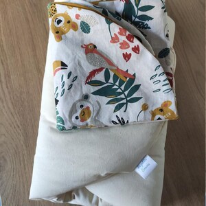 Può includere: Un tappetino da gioco bianco e crema con una copertura rimovibile colorata a tema giungla. La copertura presenta un pappagallo, scimmie e foglie. Il tappetino ha un'etichetta che dice "La Petite Souris".