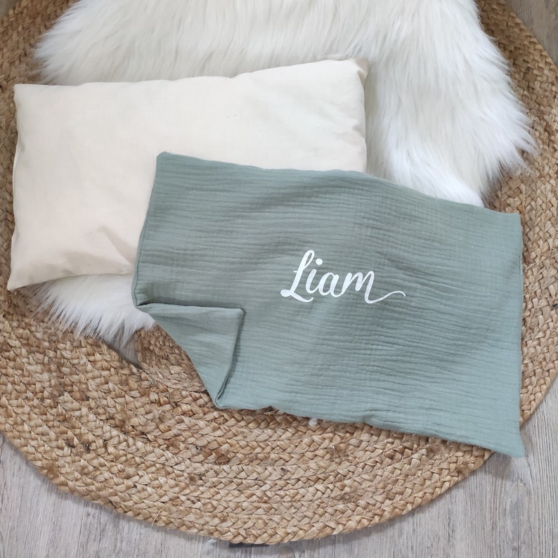 K&ouml;nnte beinhalten: Eine babygr&uuml;ne Musselin-Babydecke mit dem Namen "Liam", der in Wei&szlig; auf den Stoff gestickt ist.