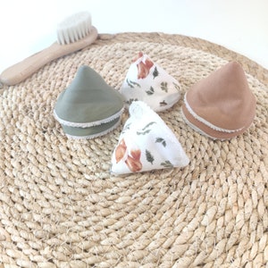 Peut inclure: Quatre coussinets réutilisables en tissu en forme de cône pour le démaquillage avec des motifs floraux. Les coussinets sont sur un tapis de paille tissé.