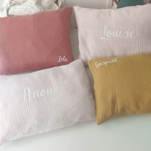 K&ouml;nnte beinhalten: Vier dekorative Kissen in verschiedenen Farben mit aufgestickten Namen. Die Kissen sind rosa, wei&szlig;, gelb und pfirsichfarben. Die Namen auf den Kissen sind "Lola", "Anouk", "Gaspard" und "Louise".