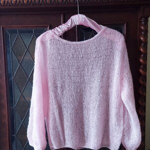 May include: A pale pink, lightweight knit sweater with a loose fit and long sleeves. The sweater is hanging on a hanger.