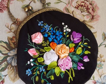 May include: A black fabric purse with a floral embroidery design. The embroidery features pink, orange, white, and blue ribbon flowers with green leaves.