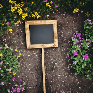 May include: A wooden framed chalkboard sign with a black surface, standing upright on a wooden stick. The sign is surrounded by purple and yellow flowers.