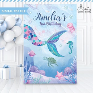Puede incluir: Una cola de sirena azul y morada con un patrón de conchas rosa y azul. La cola está rodeada de burbujas y criaturas marinas, incluyendo un caballito de mar, una tortuga y una estrella de mar. El texto "Amelia's 2nd Birthday" está escrito en blanco sobre un fondo azul.