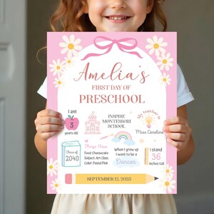 Może przedstawiać: Różowy znak z napisem "Amelia's FIRST DAY OF PRESCHOOL" jest trzymany przez dziecko. Znak zawiera szczegóły, takie jak wiek, nazwa szkoły, ulubione rzeczy i wzrost, który wynosi 91 cm. Znak jest ozdobiony stokrotkami i ołówkiem.