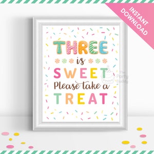 Op de afbeelding: Een wit bedrukbaar bord met kleurrijke sprinkels en de tekst "THREE is SWEET Please take a TREAT". De letters in het woord "THREE" zijn versierd met kleurrijk glazuur en sprinkels.