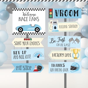 May include: A set of blue and white race car themed party signs with text that reads "Welcome Race Fans", "Vroom", "Fueling Station", "Start Your Engines", "Be Fast Or Be Last", "Rev Up And Roll Out!", "Victory Lane", "Pit Stop", and "Thanks For Racing Over".