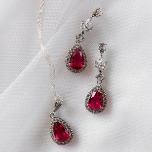 May include: A silver necklace and earrings set with red teardrop-shaped gemstones surrounded by clear cubic zirconia stones.
