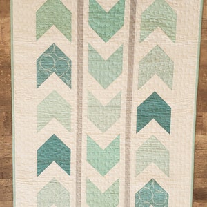 May include: A quilt with a white background and a pattern of green arrows. The arrows are made of different shades of green fabric and are arranged in rows.