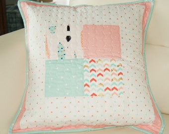 Puede incluir: Una almohada de tiro rosa y blanca con un patrón geométrico. La almohada está hecha de tela con una textura acolchada y tiene un borde azul claro.