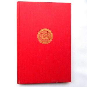 May include: A red hardcover book with a gold emblem in the center. The emblem appears to be a seal or crest with text and a central image of an open book. The book's cover is a solid, vibrant red.