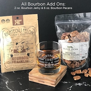 May include: A 2 oz. bag of Righteous Felon Bourbon Franklin beef jerky, a 6 oz. bag of Oliver Pecan Company bourbon praline pecans, and a clear glass tumbler filled with amber liquid, featuring the text Vintage 1945 Cheers to 80 Years.