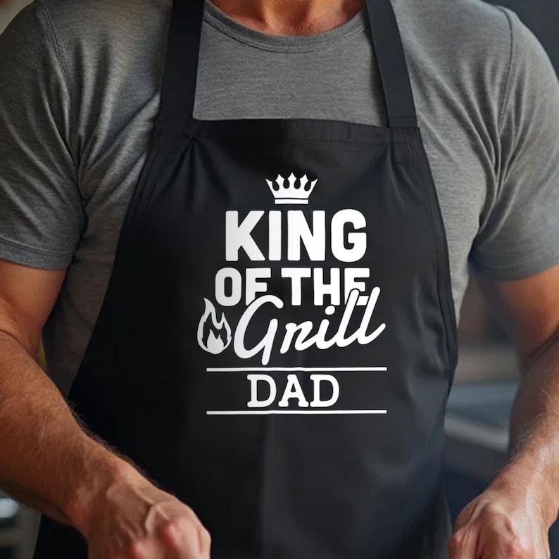 May include: Black apron with white text that reads "King of the Grill Dad" with a crown and flame graphic.