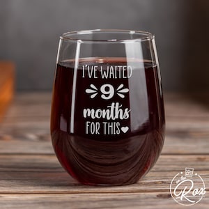 May include: A clear glass wine glass with the text "I've waited 9 months for this" etched on the side. The glass is filled with red wine.
