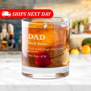 Puede incluir: Un vaso transparente lleno de un l&iacute;quido marr&oacute;n, cubitos de hielo y una cereza. El vaso tiene grabada la palabra "DAD", junto con una definici&oacute;n. Se ve una rodaja de naranja. El texto "SHIPS NEXT DAY" est&aacute; en una pancarta roja.