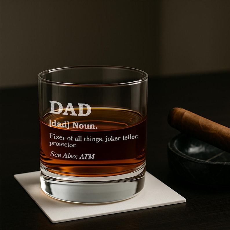 Puede incluir: Un vaso transparente con la palabra "DAD" grabada en la parte delantera, lleno de l&iacute;quido &aacute;mbar. Debajo de la palabra "DAD" est&aacute; la definici&oacute;n: "Arreglador de todo, cuentachistes, protector. Ver tambi&eacute;n: ATM."